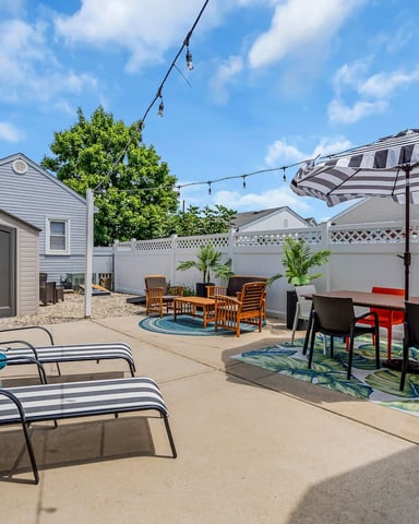 Backyard patio with striped lounge chairs, dining table under umbrella, storage shed, and white privacy fence