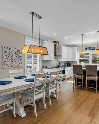 Open-plan dining and kitchen with white cabinetry, wood flooring, pendant lights, and ocean views through multiple windows.