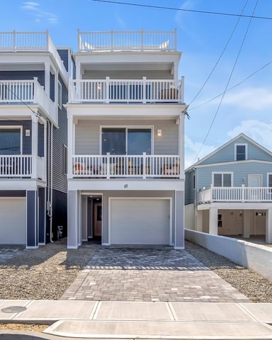 Modern multi-story beach houses with white railings, decks, and garage doors on paved driveway