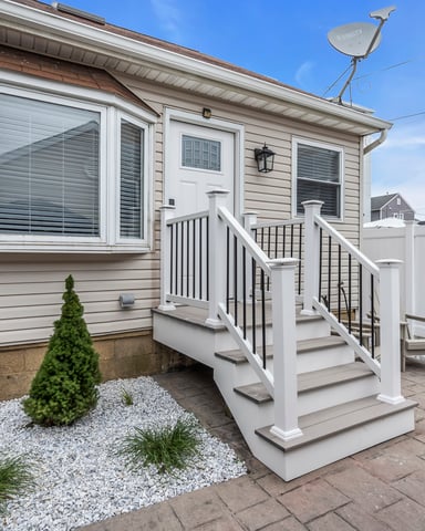 Cozy exterior of a shore rental home with white staircase, decorative landscaping, and welcoming entrance