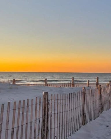 Sandy beach at sunset with wooden dune fences and calm ocean horizon