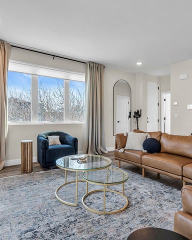 Modern living room with leather sectional sofa, glass coffee table, and large windows with natural light