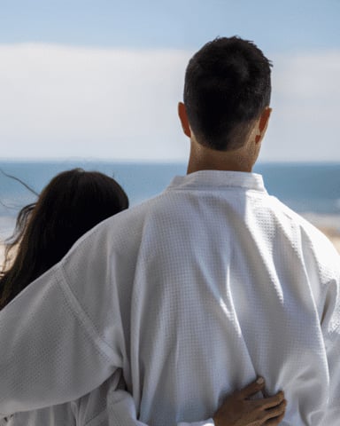 Couple standing on grassy overlook facing ocean beach and horizon