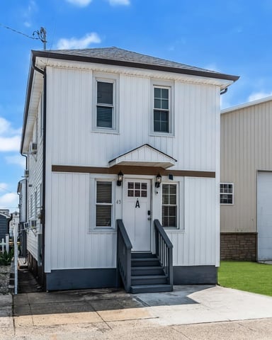 White metal-sided house with black trim and front steps, adjacent garage, clear blue sky