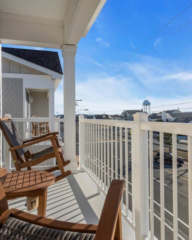 Elevated deck with white railing, wooden rocking chairs, overlooking parking lot and residential neighborhood under clear blue sky