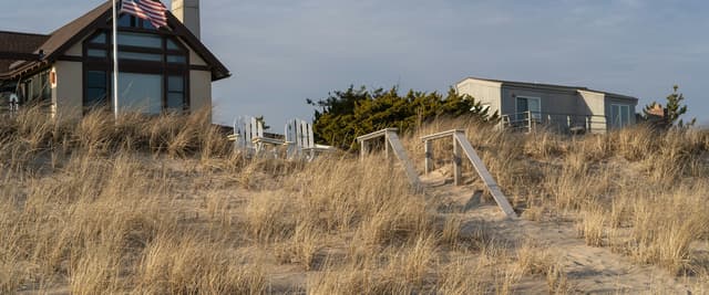 Shore homes rising above dune grass with an American flag and Adirondack chairs in warm golden light