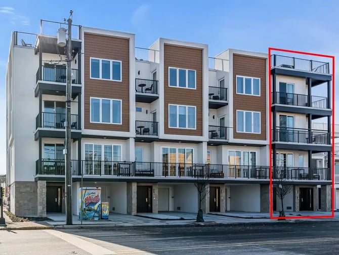 Modern multi-story residential building with brown and white facade, ground-floor retail spaces, and black metal balconies